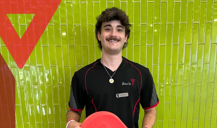 Wesley, the lifeguard, stands in front of a green wall with a smile on his face