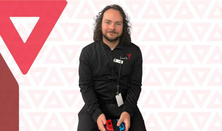 Kurt Robertson, YMCA Calgary Esports Supervisor, smiling while holding a gaming controller 