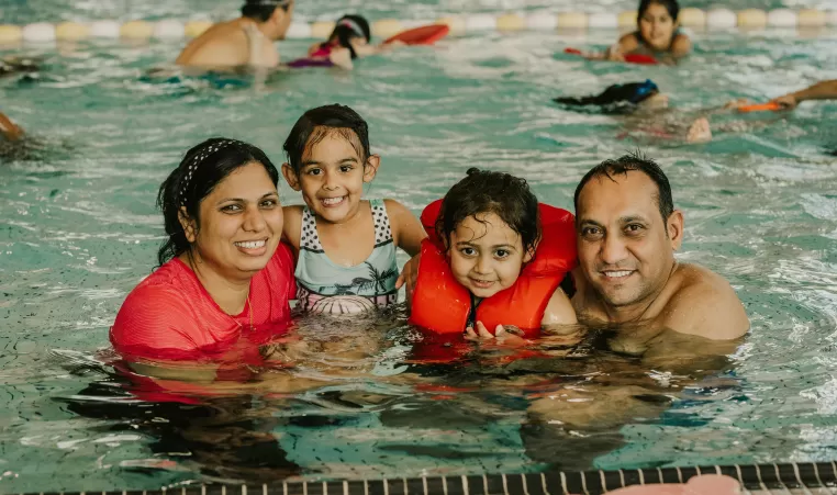 Family of four in the pool together smiling at camera. 