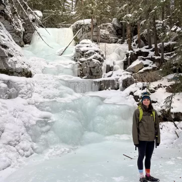 YMCA Staff member Kyla stands next to a frozen waterfall on a winter hike