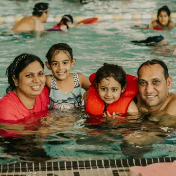 Family of four in the pool together smiling at camera. 